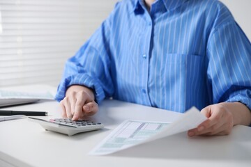Fototapeta premium Budget. Woman with paperwork and calculator at white desk indoors, closeup