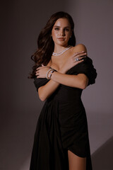 beautiful slavic woman with dark curly hair in luxurious black evening dress with jewelry posing in...