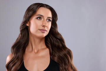 Obraz premium Hair styling. Beautiful woman with wavy long hair on grey background, space for text