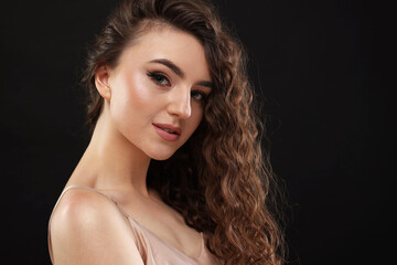 Fototapeta premium Beautiful young woman with long curly brown hair on black background, space for text
