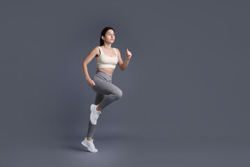 Woman in sportswear exercising on grey background