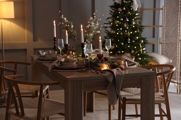 Christmas table setting with stylish dishware, glasses and burning candles in festive decorated room
