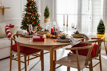 Christmas table setting with stylish dishware, glasses and burning candles in festive decorated room