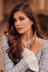 beautiful slavic woman with dark curly hair wears elegant blue tweed jacket with jewelry, posing in...