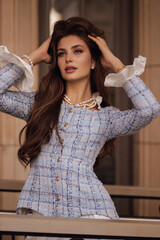 beautiful slavic woman with dark curly hair wears elegant blue tweed jacket with jewelry, posing in...
