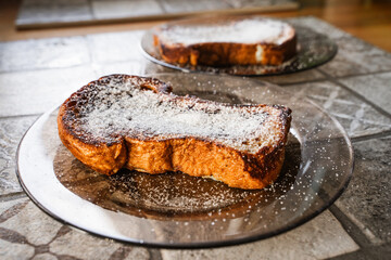 Fried French toast with white sugar on a round plate in the home kitchen setting. Close-up side view of sweet bread croutons for breakfast. Selective focus.