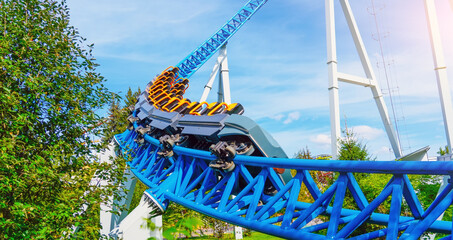 Roller coaster cart with people riding goes through the cart rises high into the air before descending turn sharply into steep dive against backdrop blue sky and clouds © aapsky