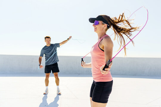 Adults skipping rope during a sunny workout session on a rooftop in an urban area