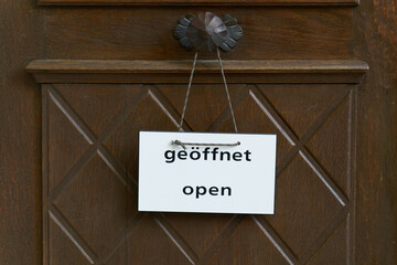 Schild an einer Eingangstür mit dem Wort offen, open in deutscher und englischer Sprache