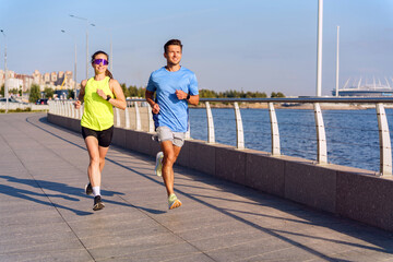 Fototapeta premium Joggers enjoying a sunny day along a waterfront promenade in the city