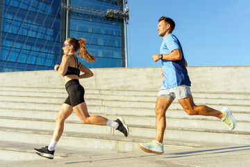 Fototapeta premium Couple jogging on outdoor steps near modern architecture during bright afternoon sunlight