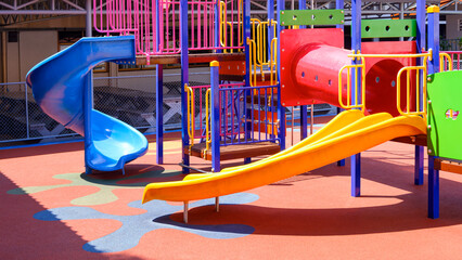 Colorful slide with playground climbing equipment on rubber floor in outdoors playground area at...