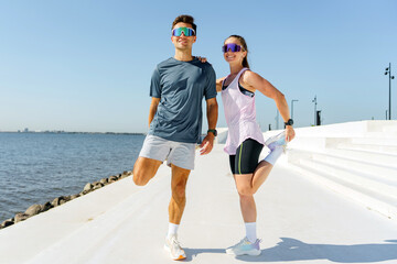 Couple enjoying outdoor fitness by the waterfront while stretching under a clear blue sky