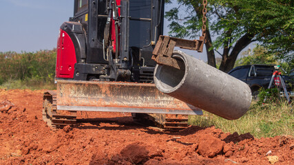 Excavators use chains and hooks to lift and move concrete drainage pipes into the soil in road construction.