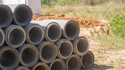 Concrete pipes are stacked on the ground in front of a road construction site. to prepare for drainage pipes