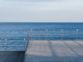Obraz premium Plank ledge with handrails by the sea against the background of a blue clear sky. Concept of rest, trip, relaxation, vacation