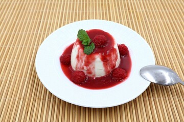 Panna Cotta with raspberry coulis, raspberries and mint on a white plate on a wooden background. Tasty dessert.