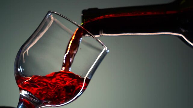 Alcohol. Wine. Red vine is pouring from bottle into goblet. Close-up of red wine forms