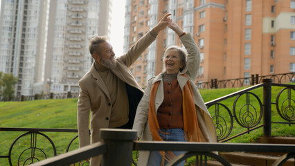 Carefree mature Caucasian couple grandparents family dancing romantic anniversary together dance in city park happy 60s aged older woman man moving outdoors loving happy male female partners in love