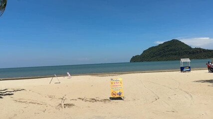 Serene coastal scene of tall trees with signages on the sunlit Sam Roi Yot Beach in front of sea