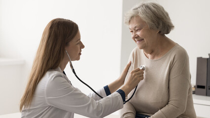 Trusted doctor. Caring young lady medical professional cardiologist check cardio health of senior aged grandmother patient visiting doc at hospital office listen heartbeat rate lungs using stethoscope