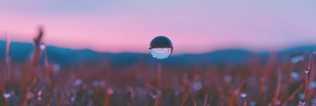 Single large droplet reflects blurred landscape with soft colors and gradients in background