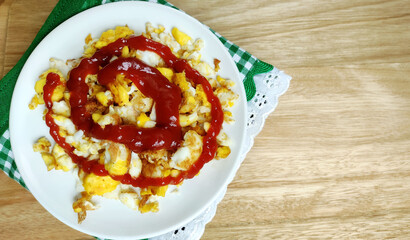 Healthy meal with scrambled eggs and ketchup on the decorated cloth on the wooden table in homely atmosphere
with copy space.