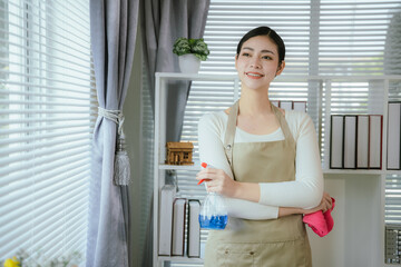 A professional maid in uniform tidies up an office space, wiping surfaces with a rag and spray....