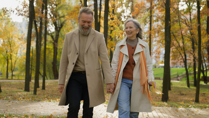 Happy Caucasian family retired married couple 60s old mature woman man going walking in city park...