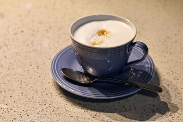 fresh cappuccino or coffee with milk in a blue cup and teaspoon