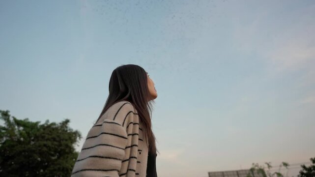 Asian woman looking at flock of bats flying from cave in the evening