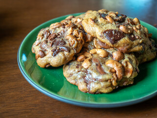 Home made big crunchy soft chocolate cookies with cashew nuts fresh baked on green plate on wooden dining table