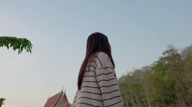 Asian woman looking at flock of bats flying from cave in the evening