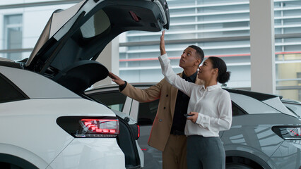 Auto dealer woman demonstrate customer automatic opening trunk new modern electric transport in...