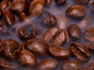 Black coffee beans with light smoke from steam, texture of coffee beans