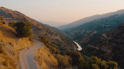 Fototapeta premium Winding road through a scenic valley with mountains and a river in the background during sunset.