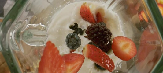 Extreme close-up view of mix fruits dropping on milk inside the blender, process of making smoothie with fruits and milk
