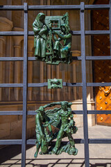 A close-up of a metal gate with ornate, sculpted figures depicting scenes of daily life, with a...