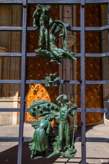 A close-up shot of an ornate metal gate with sculpted figures in dynamic poses, set against a...