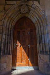 An ornately carved wooden door with metal hardware is set within a weathered stone archway,...