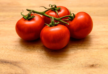 Four ripe red tomatoes are arranged on a wooden table, showcasing their vibrant color and fresh appearance, ideal for salads and cooking