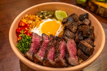 Grilled beef steak rice bowl with fried egg in Thai fusion Asian style served with chilli and lime