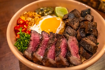 Grilled beef steak rice bowl with fried egg in Thai fusion Asian style served with chilli and lime