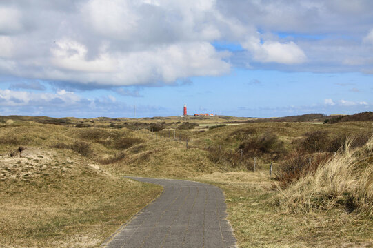 una stradina che si perde tra le dune erbose e il faro rosso di De Muy sull'isola di Texel in Olanda