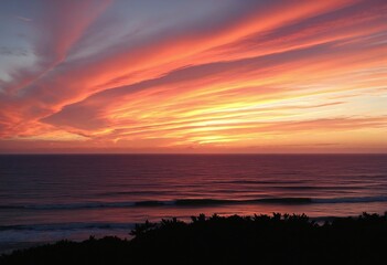 Fototapeta premium A stunning summer evening sky ablaze with orange and pink colors reflected over the tranquil ocean.