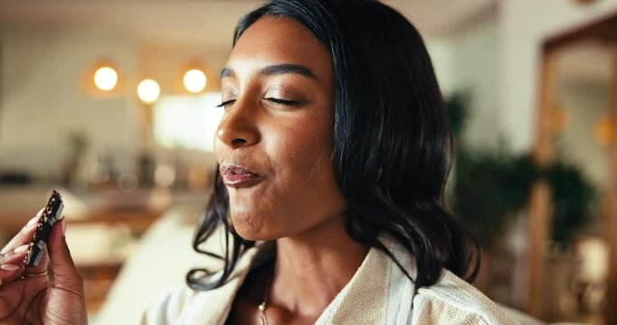 Woman, eating chocolate and relax in home, comfort food and craving cacao nutrition in living room. Female person, eyes closed and sweet sugar snack to enjoy, dessert and bite of dark gourmet candy
