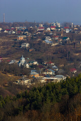 View of a hillside village featuring houses and a church, set against a backdrop of serene hills and a clear sky during daytime