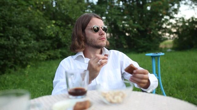 A man with long hair savors chocolate in the garden
