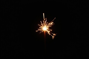 Fototapeta premium A single burning sparkler against a dark background, radiating bright light and creating a celebratory atmosphere.