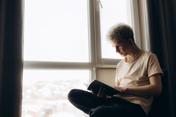 Young Man Reading a Book by a Bright Window Light